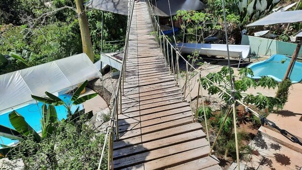 A wooden suspension bridge over a pool area with lounge chairs and umbrellas. - Relaxing Luxury Jungle Escape in Quepos with Jacuzzi, Zipline, Pool and more (Parrita)