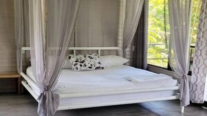 A four-poster bed with sheer curtains, a white mattress, and a patterned pillow. - Relaxing Luxury Jungle Escape in Quepos with Jacuzzi, Zipline, Pool and more (Parrita)