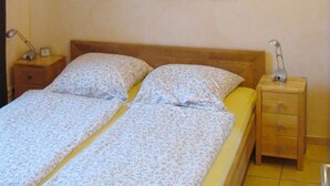 A double bed with floral bedding, a nightstand with a lamp, and a wall-mounted painting of a desert landscape. - bright terrace apartment with beach chair in the old captain's house, max. 3 pers. (Prerow)