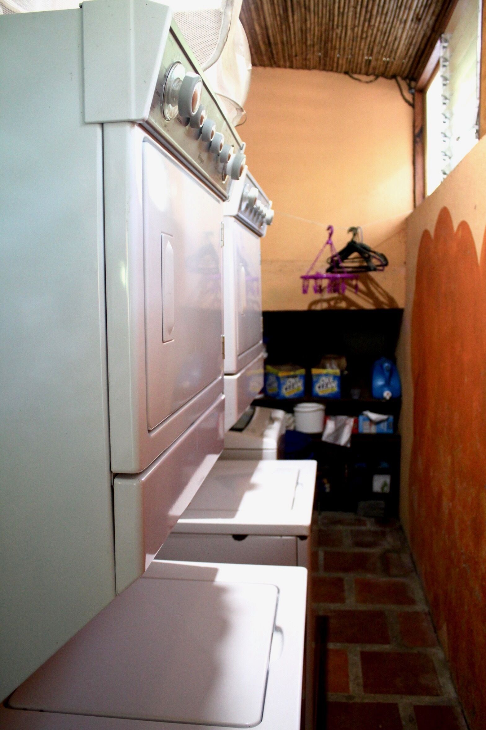 Un espace buanderie avec des machines à laver et des sèche-linge superposés, un mur en briques et une étagère contenant des produits de nettoyage.