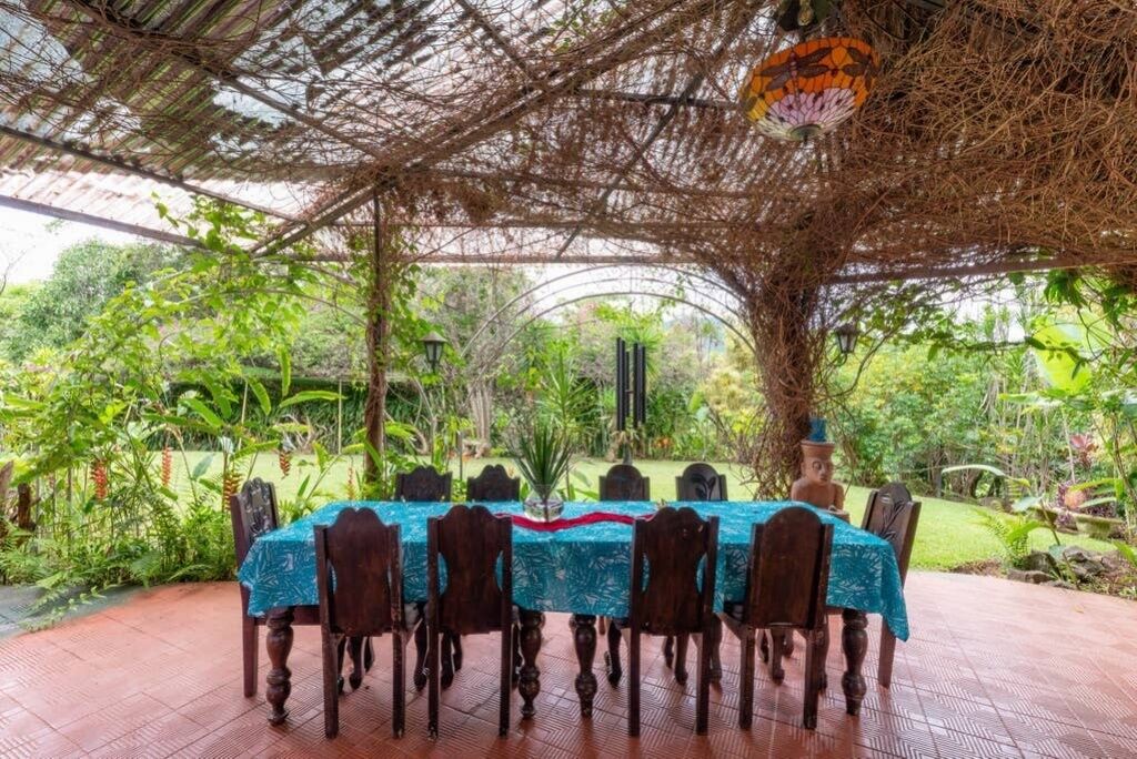 Un área de comedor al aire libre con una mesa cubierta por un mantel azul y rodeada de sillas de madera.
