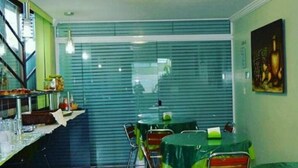 A dining area with tables covered in green tablecloths, chairs, and a counter with food items. - Pousada Belo Horizonte (Macaé)