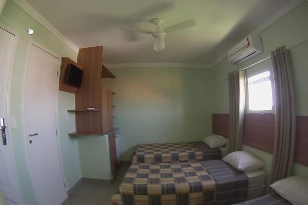 Un dormitorio pequeño y sencillo con dos camas, un ventilador de techo y un televisor montado en la pared.