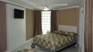 A bedroom with a bed, a television on the wall, and a window with curtains. - Pousada Belo Horizonte (Macaé)