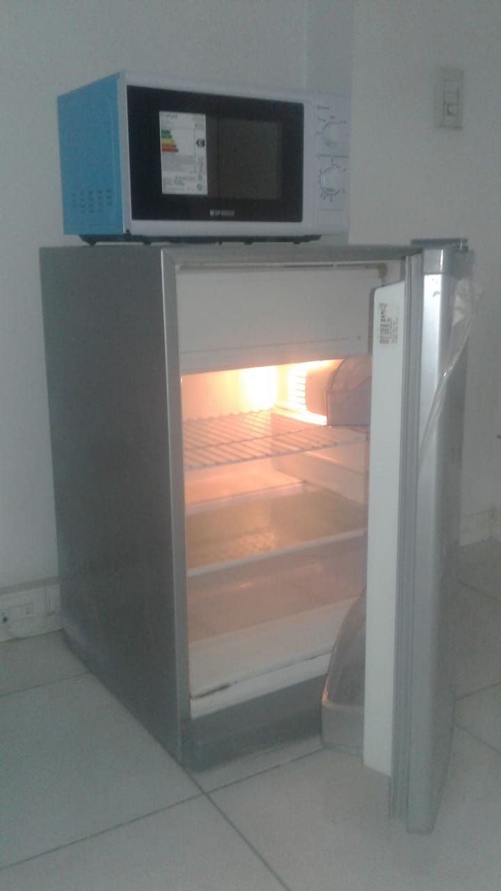 Un refrigerador compacto con un microondas encima, ubicado en una habitación con paredes blancas y piso de baldosas.