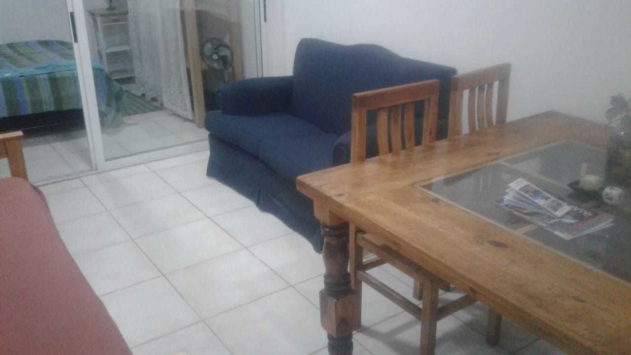 A room with a wooden dining table, a blue sofa, and a glass coffee table.