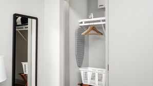 A modern bathroom with a mirror, a white laundry basket, a hanging iron, and a white towel rack. - Studio King Suite with Kitchen | 203 (Asheville)