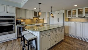 A kitchen with white cabinets, a central island with stools, stainless steel appliances, and pendant lighting.