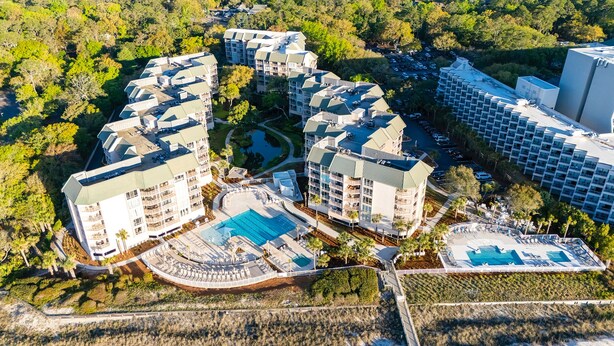An aerial view of a resort with multiple buildings, a central pool, and surrounding greenery.