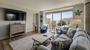 A living room with a sofa, armchairs, a coffee table, and a TV mounted on the wall.