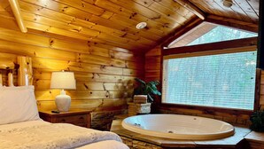 Quarto de cabana de madeira aconchegante, com uma banheira de pedra, cama com roupa de cama branca e janela com persianas.
