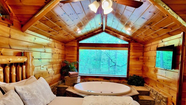 Quarto acolhedor de cabana de madeira com uma cama grande, uma banheira de hidromassagem e vista para a floresta pela janela.
