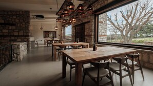 Un'ampia sala da pranzo con un grande tavolo di legno e sedie, pareti in pietra e vista sull'esterno tramite un'ampia finestra.