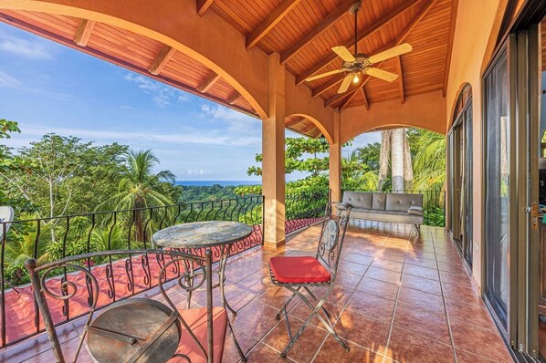A covered outdoor area with a table and chairs, a ceiling fan, and a view of lush greenery. - Jungle Dream- Magnificent Getaway with Ocean-Mountain Views (Savegre)