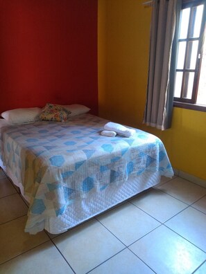 A bed with a quilt, pillows, and a rolled towel.