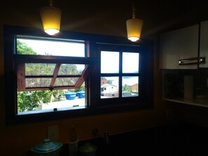 A kitchen with a large window, two hanging light fixtures, and a view of the outside.