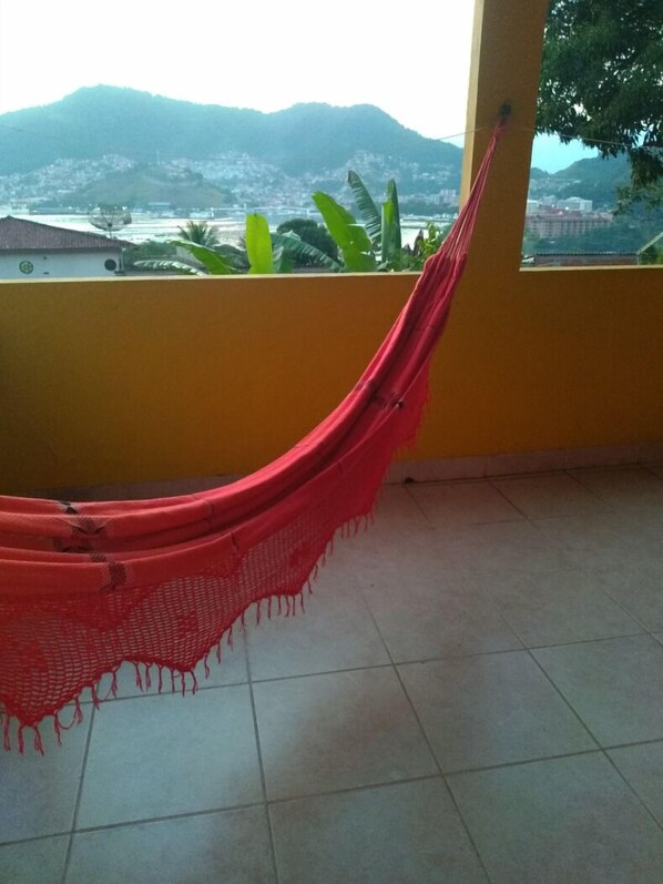 A hammock on a balcony with a view of mountains and greenery.