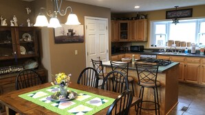 A kitchen with wooden cabinets, a dining table with chairs, a central island, and a hanging light fixture.