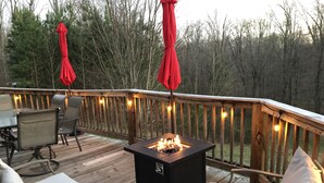 A wooden deck with outdoor seating, a fire pit, and string lights.