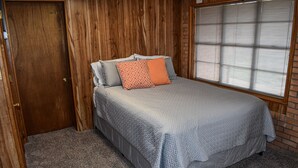 A bedroom with a bed, a wooden door, and a window with blinds. - The Cozy Buffalo near Palo Duro Canyon & WTAMU (Canyon)