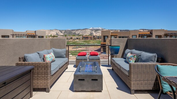 A rooftop patio with wicker furniture, a glass-top table, and a view of mountains. - 2 Much Fun (St. George)