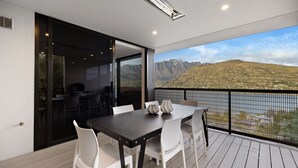 Een balkon met een tafel, stoelen, een barbecue en uitzicht op bergen en een meer.