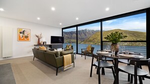 Een moderne woonkamer met een bank, televisie en eethoek met een tafel gedekt voor twee personen, met uitzicht op een bergmeer.