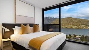 Een moderne hotelkamer met een groot bed, uitzicht op bergen en een meer, en een kunstwerk in een lijst aan de muur.