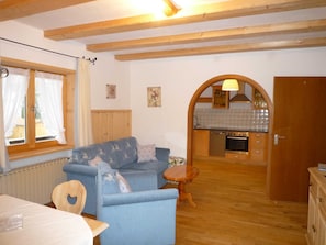 A cozy room with a sofa, a small wooden table, a kitchen area with a stove and cabinets, and a window with curtains.