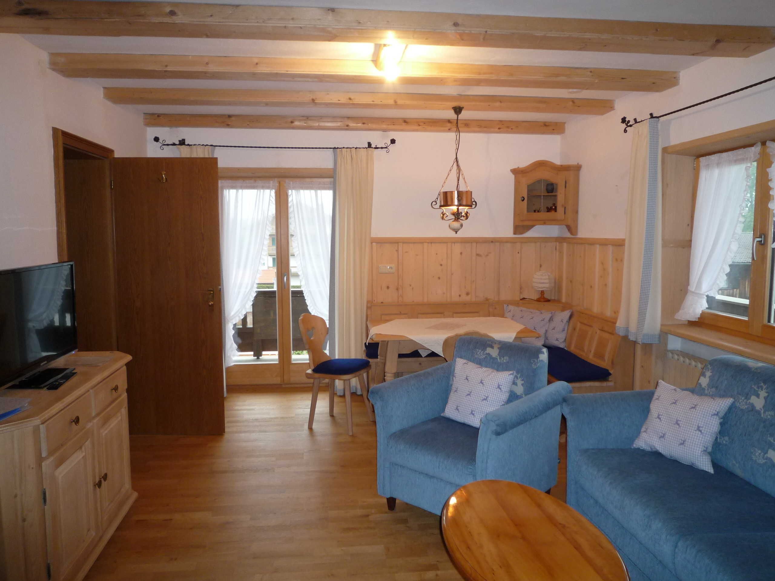 Une pièce chaleureuse avec des poutres apparentes, une télévision, un canapé, une table en bois et un coin repas comprenant une table et des chaises.