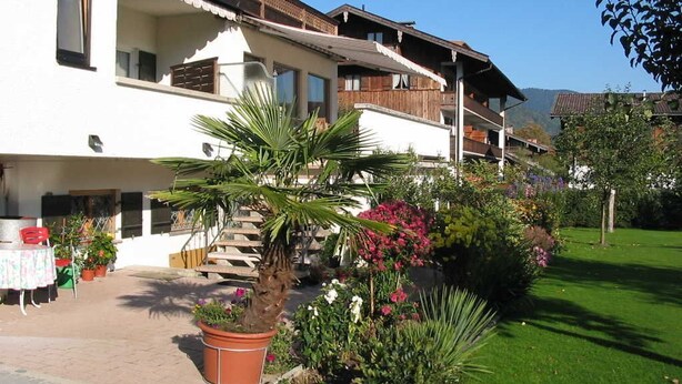 Un edificio de varios pisos con balcones, una escalera y un jardín con diversas plantas y flores.