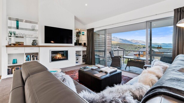 Un salon moderne doté d’une cheminée, d’un grand téléviseur à écran plat et d’un balcon offrant une vue sur les montagnes.