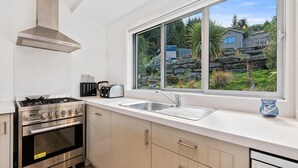 Une cuisine moderne équipée d’une cuisinière à gaz, d’un four et d’une grande fenêtre donnant sur un paysage rocheux et une maison.