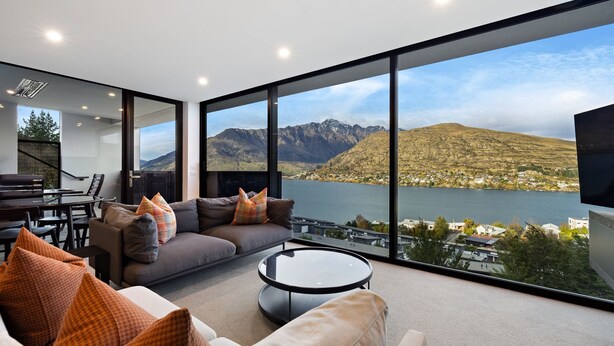 A modern living room with a large window offering a scenic view of mountains and a lake.