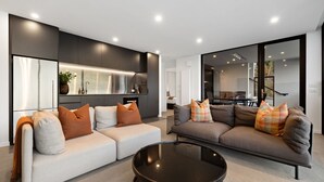 A modern living room with a grey sofa set, a black coffee table, and a large window offering a view of the outdoors.