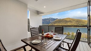 A balcony with a wooden table set for dining, overlooking a mountainous landscape.