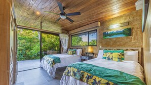 Habitación con dos camas, ventilador de techo y ventanas amplias con vistas al exterior.