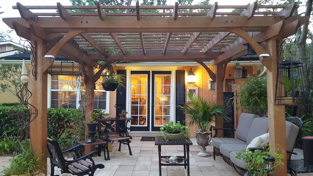 A covered patio area with wooden furniture, potted plants, and a view of the interior through a glass door. - Intercostal Waterfront Private Cottage Retreat Close to Mayo Clinic (Jacksonville)
