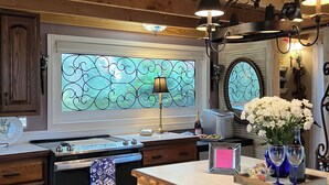 A kitchen with wooden cabinets, a stainless steel oven, a large window with a stained glass design, and a chandelier. - Intercostal Waterfront Private Cottage Retreat Close to Mayo Clinic (Jacksonville)