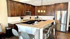 A modern kitchen with wooden cabinets, a stainless steel refrigerator, a central island with bar stools, and a hanging light fixture. - Spinnaker Point #2 - BEACH FRONT! Come Stay At Our Lake House in Bear Lake, Utah! (Garden City)