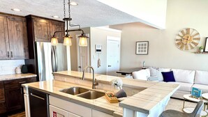 A modern kitchen with a central island, stainless steel appliances, and a dining area with a sofa and chairs. - Spinnaker Point #2 - BEACH FRONT! Come Stay At Our Lake House in Bear Lake, Utah! (Garden City)
