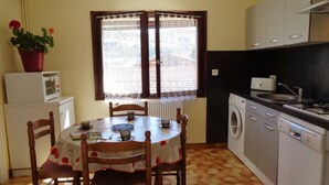 A compact kitchen with a dining table, chairs, a washing machine, and a microwave.