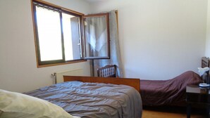 A bedroom with a bed, a chair, a desk, and a window with curtains.