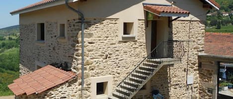 Una casa in pietra con tetto in tegole rosse, una scala che conduce a un balcone e vista sulla campagna.