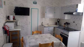A compact kitchen with white cabinets, a small dining table, a microwave, a kettle, and a sink.