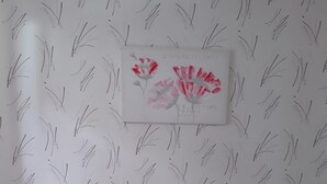 A bedroom with a bed, two nightstands, a red vase, and a wall with a floral pattern.