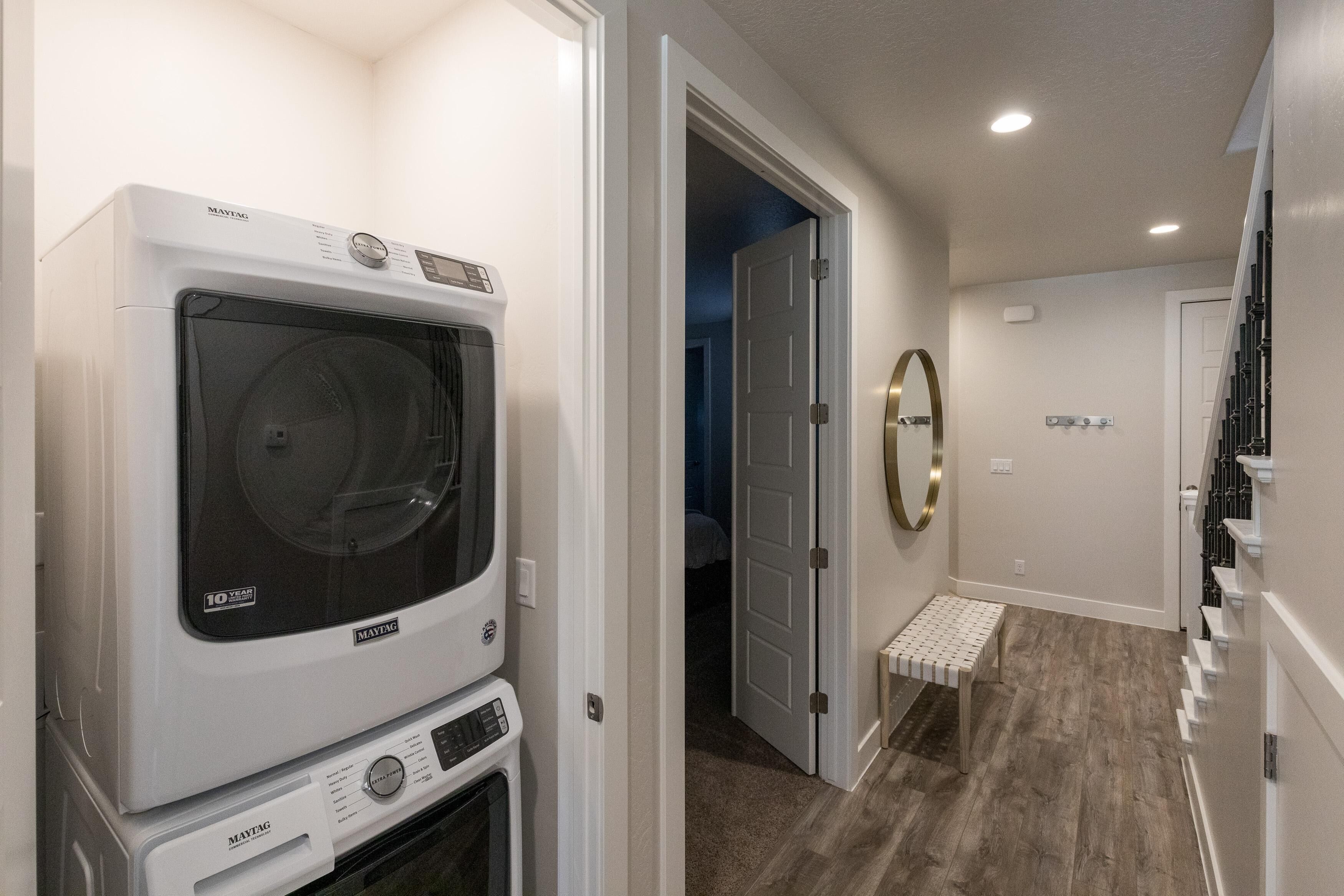 A laundry area with stacked washers and dryers, a bench, and a door leading to another room.