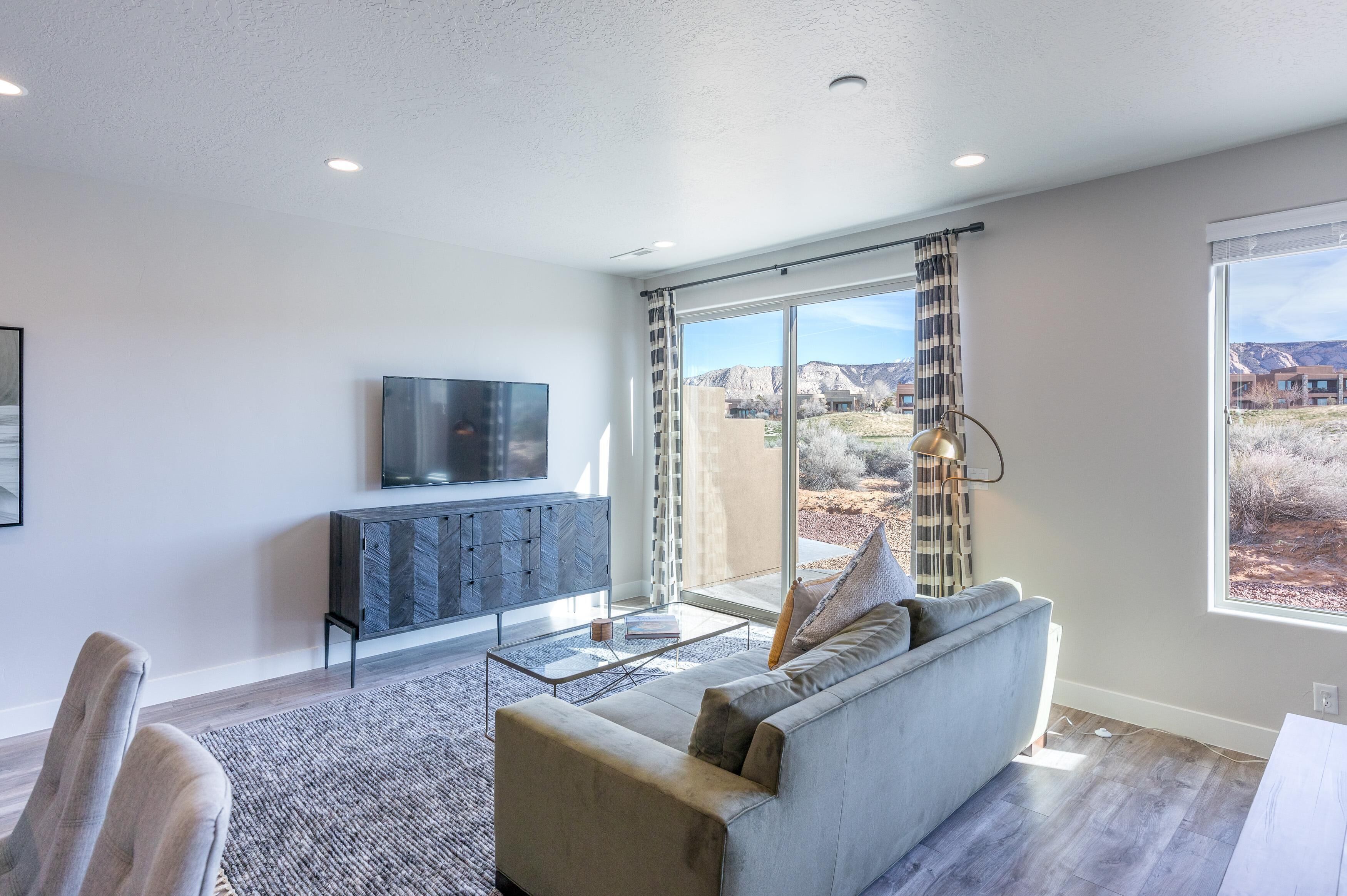 A modern living room with a sofa, coffee table, and TV, large windows with a mountain view, and a herringbone-patterned cabinet.