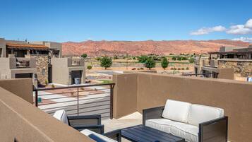 A rooftop patio with outdoor furniture, a view of a desert landscape, and a mountain range in the background.
