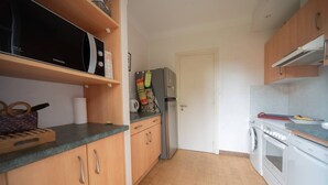 Ett kompakt kök med träskåp, en mikrovågsugn, ett kylskåp, en tvättmaskin och ett handfat.